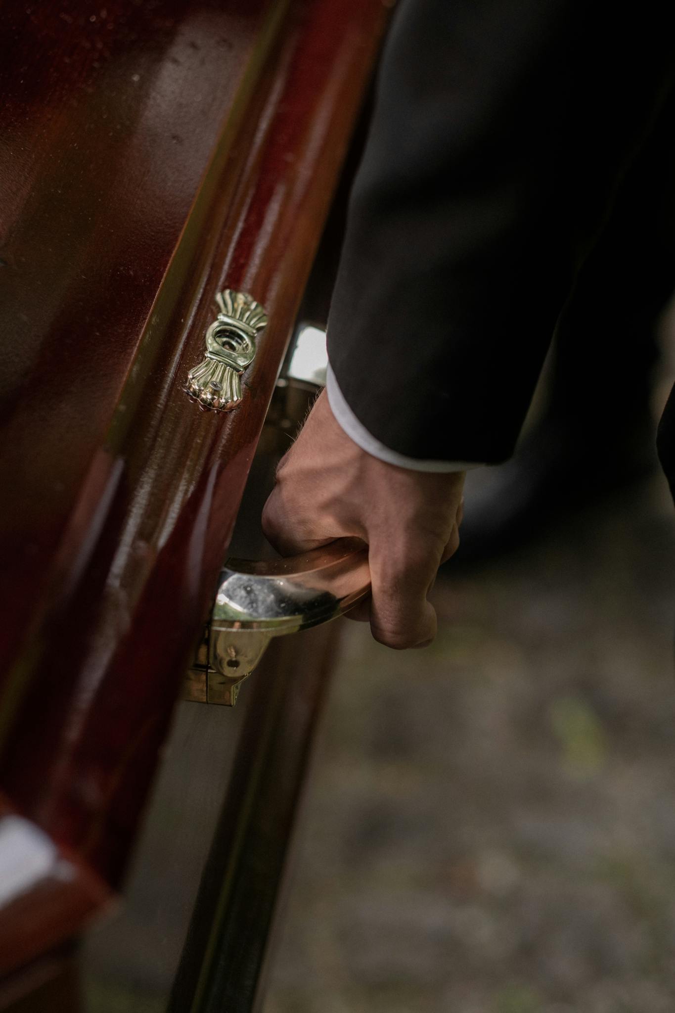 Close-up of a hand holding a wooden casket handle during a funeral ceremony.