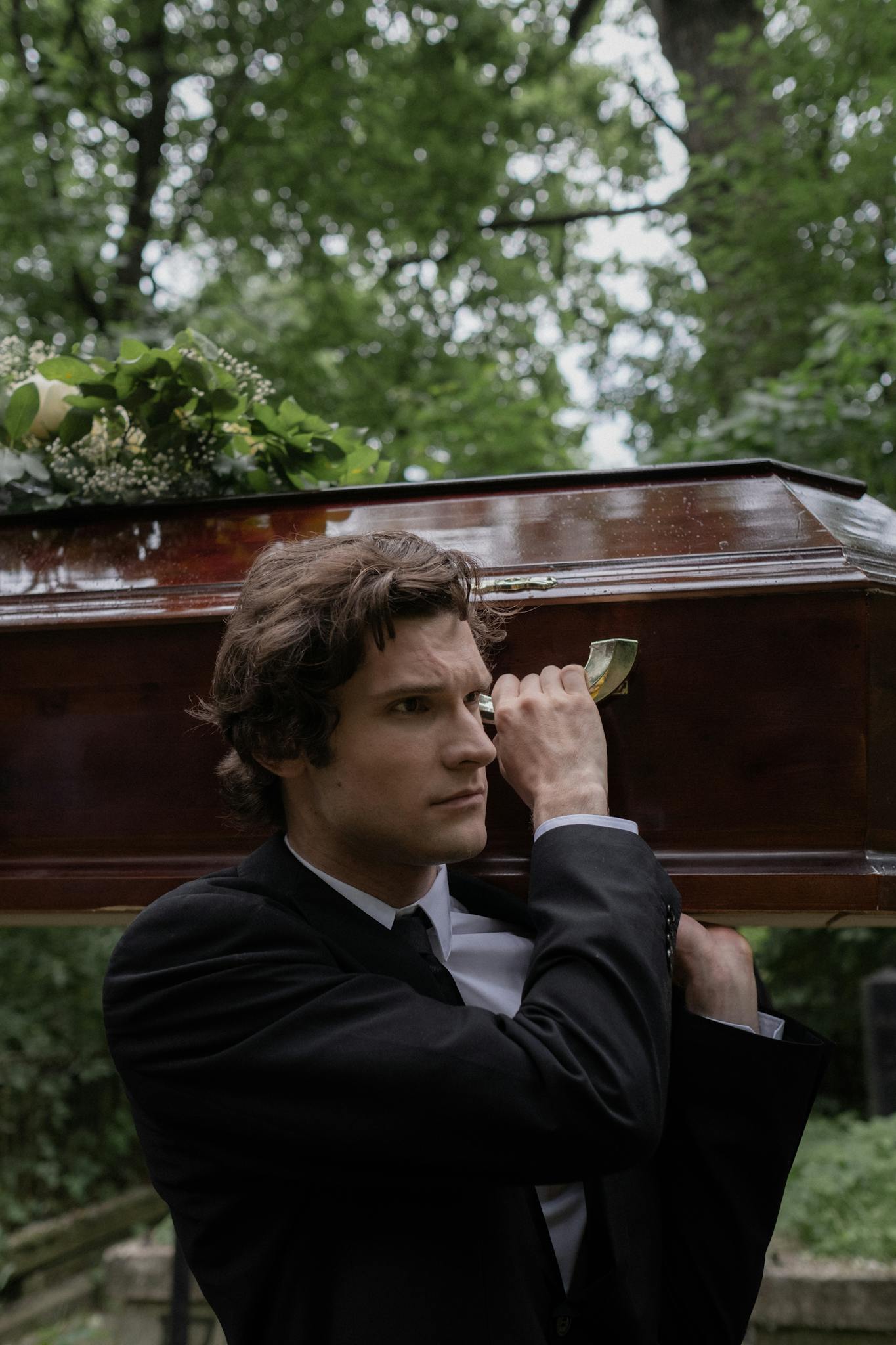 Solemn moment as man carries a coffin in a lush cemetery, symbolizing loss and remembrance.